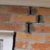 A brick wall displaying stair-step cracks and messy tuckpointing on a Huntsville home